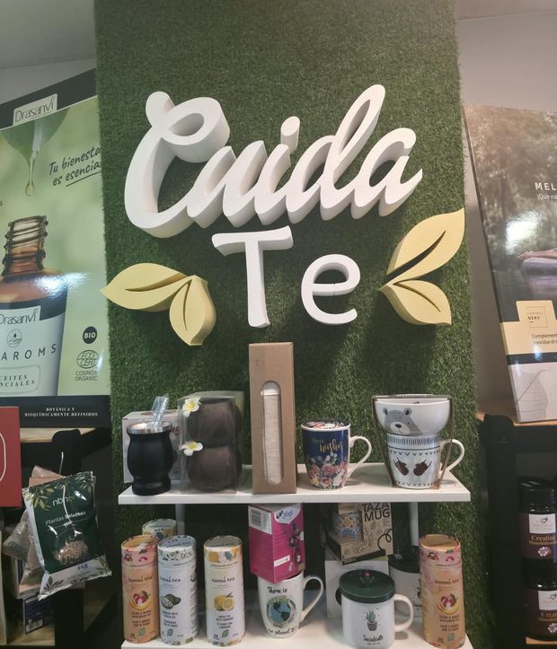 La pared de césped de la tienda con el letrero Cuida Te y tazas en baldas blancas.